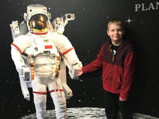 A student is shown in front of an exhibit shaking hands with an astronaut.
