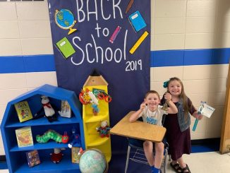 Students pose in front of a back to school decorated door and desk.