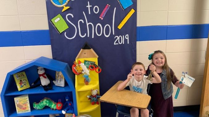 Students pose in front of a back to school decorated door and desk.